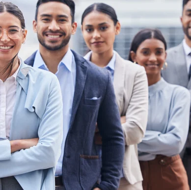 A group of five diverse professionals in business attire stand in a line, smiling at the camera.