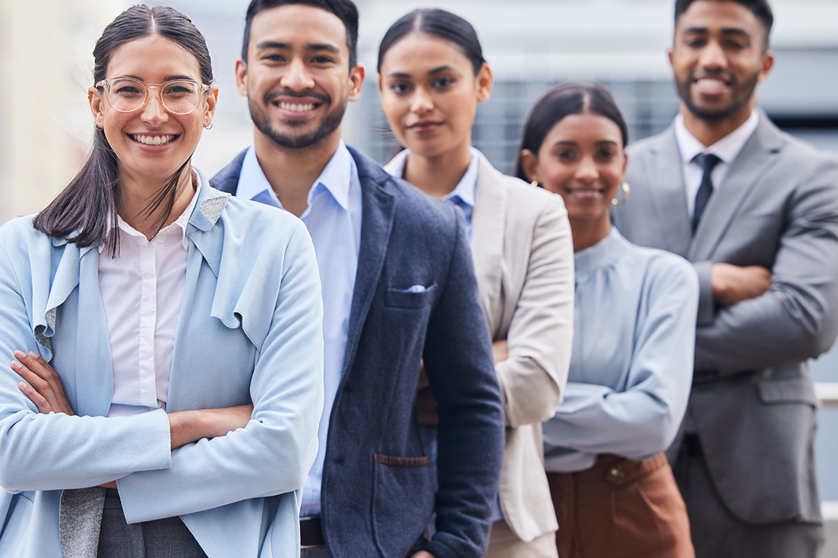 A group of five diverse professionals in business attire stand in a line, smiling at the camera.